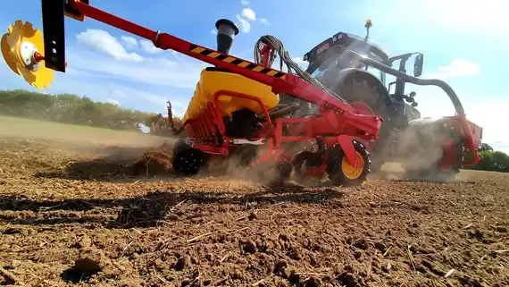 Traktor zieht eine rote Landmaschine über ein staubiges Feld unter blauem Himmel. (automatisch generiert durch KI)