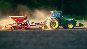 Traktor mit Anhänger pflügt ein Feld, umgeben von unscharfen Bäumen im Hintergrund. (automatisch generiert durch KI)