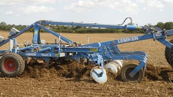 Ein blauer Lemken-Pflug bearbeitet ein Feld unter einem bewölkten Himmel. (automatisch generiert durch KI)