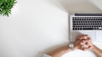 Hände einer Person auf einem weißen Tisch neben einem Laptop und einer Pflanze. (automatisch generiert durch KI)