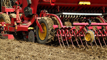 Roter landwirtschaftlicher Sämaschine bearbeitet einen Ackerboden. (automatisch generiert durch KI)