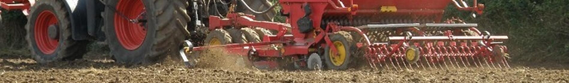 Traktor mit Sämaschine bearbeitet ein Feld, umgeben von Bäumen. (automatisch generiert durch KI)