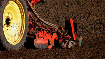 Ein Traktor pflügt ein Feld. Nur das Rad und ein Teil des Pflugs sind sichtbar. Die Erde ist dunkelbraun und frisch gepflügt. (automatisch generiert durch KI)