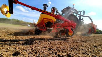 Traktor zieht eine rote Landmaschine über ein staubiges Feld unter blauem Himmel. (automatisch generiert durch KI)